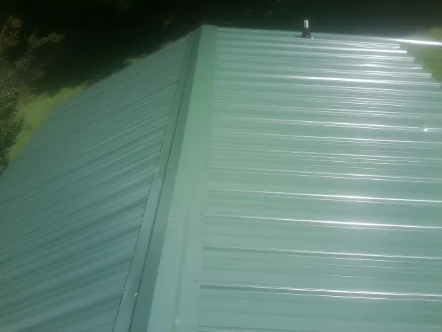 New green metal panels meeting at the ridge of a roof — Flat Roof Repair work by our crew in Clementon