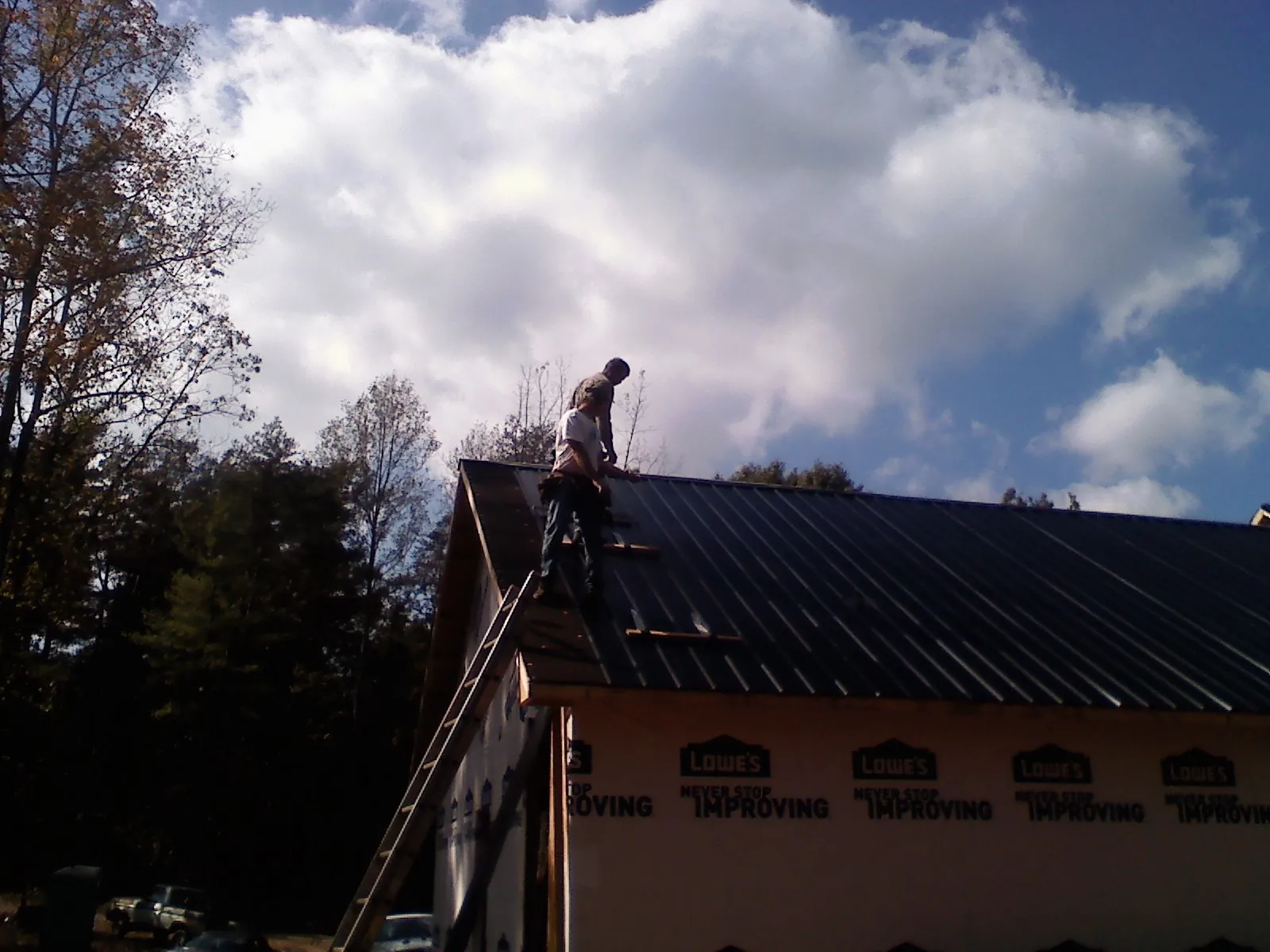 Roofer fastening dark metal panels high against a cloudy sky, from a Roof Inspection job in Clementon