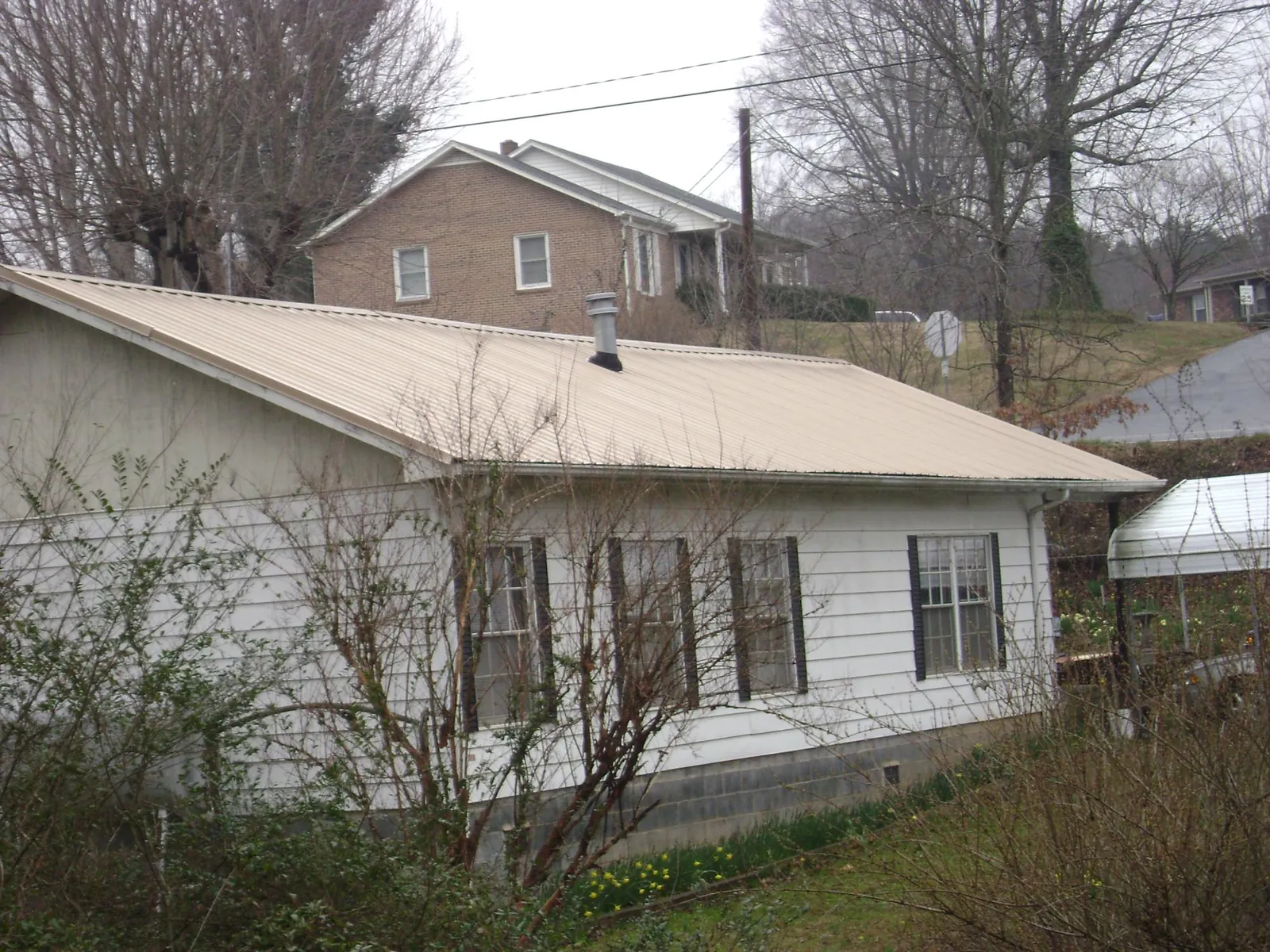 Tan metal roof on a white sided house set into a hillside — Commercial Roofing by Roofing Brothers in Clementon